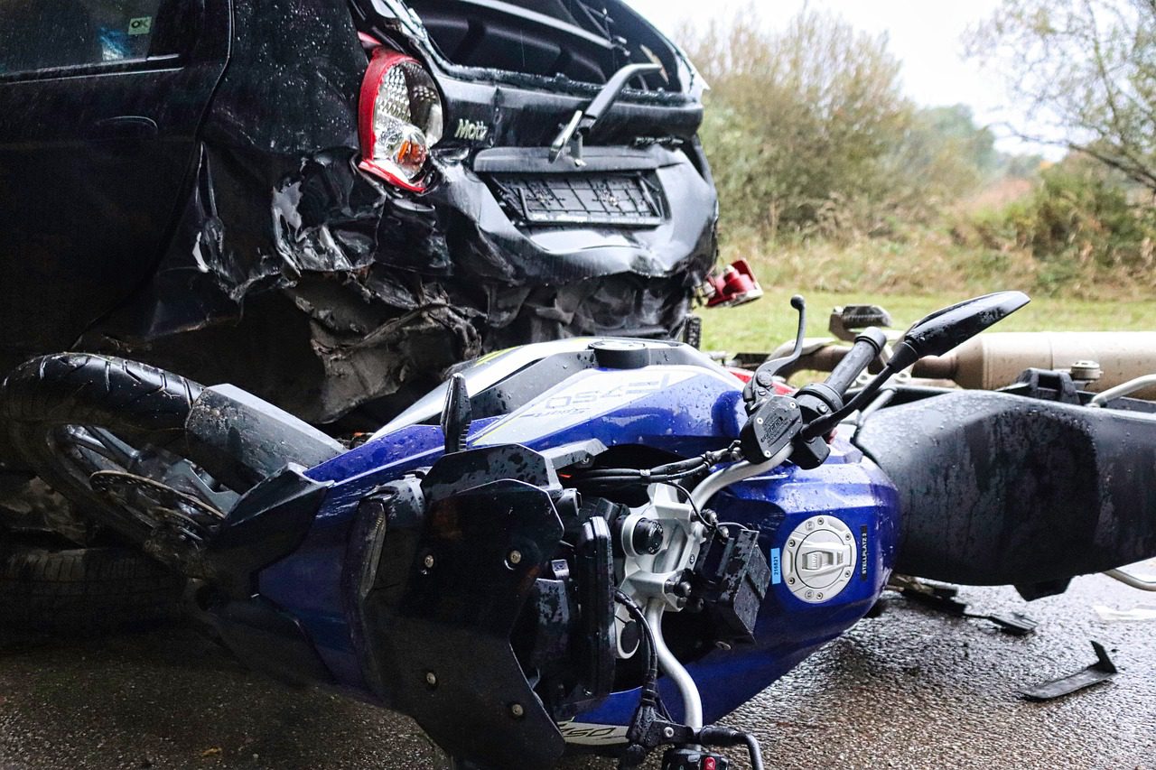 A black car and a blue motorcycle collided on a wet road near the green grass