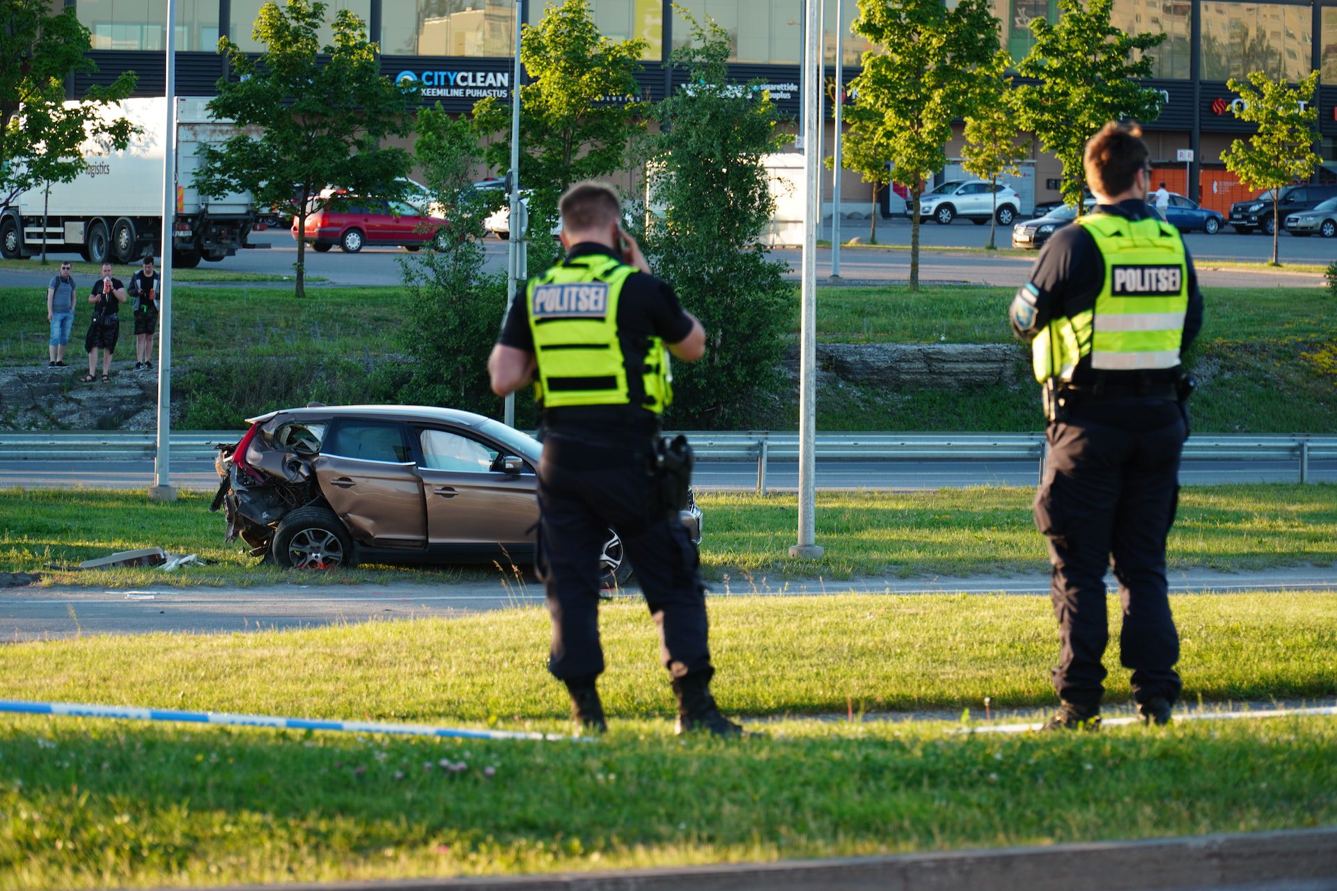 Two police officers wearing neon green vest stands near a brown car on a green grass