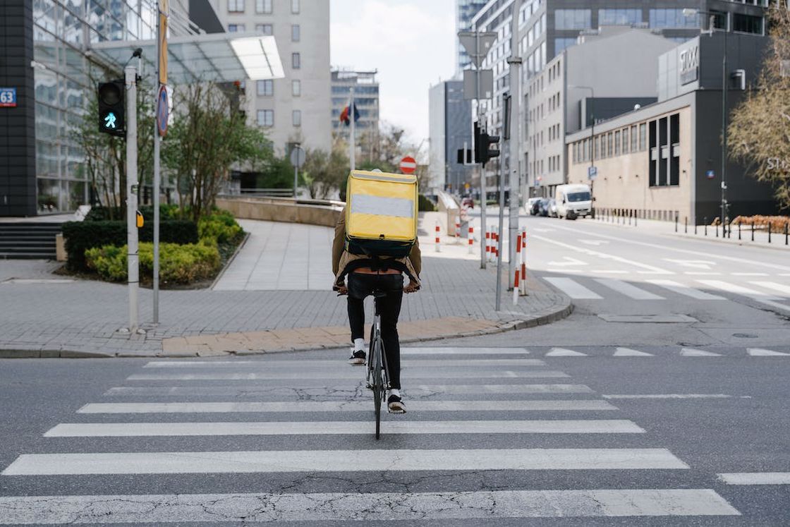 Man on a bicycle with a yellow storage compartment attached on his back while crossing the road