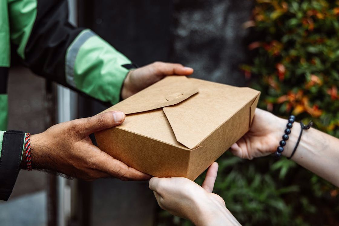 Man wearing a green jacket handing out a brown food box to a customer