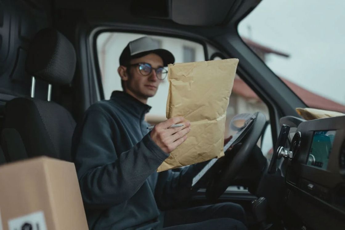 Delivery driver checking the details of a brown parcel while sitting on his truck