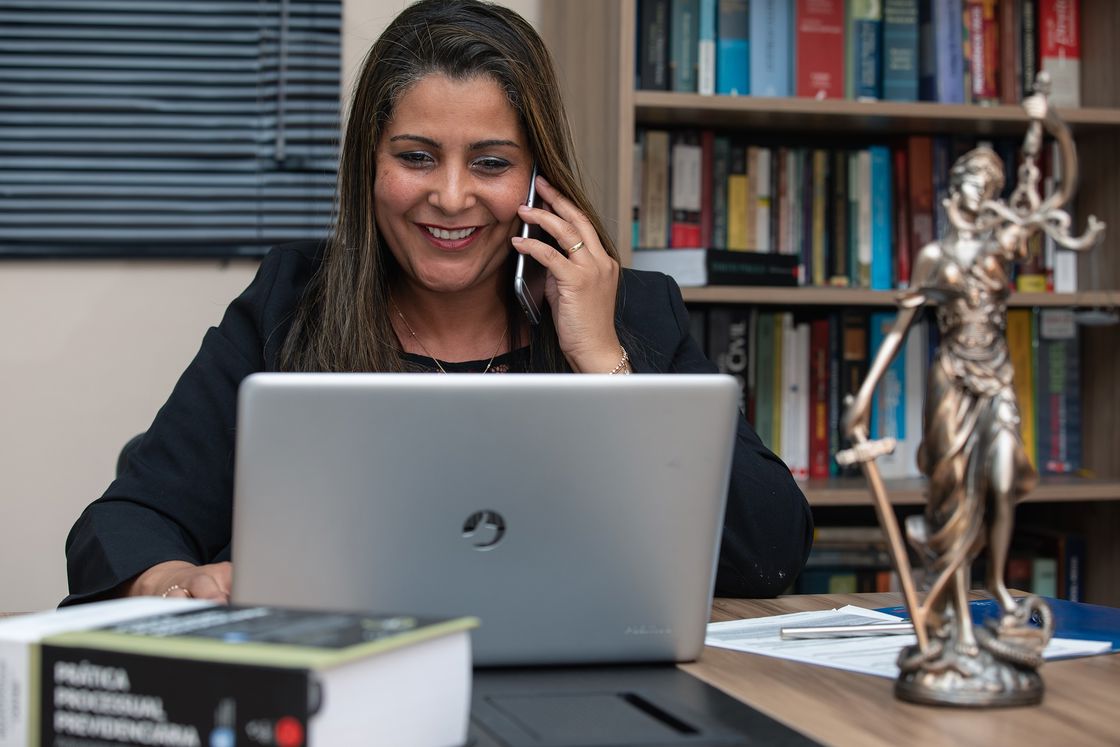 Attorney talking on her cellphone while looking at her laptop while working on her office