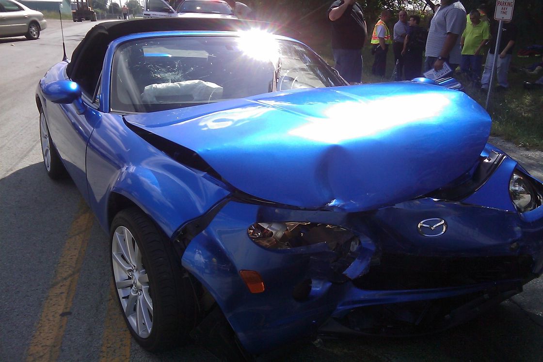 Blue car with a badly damaged front end parked beside the sidewalk