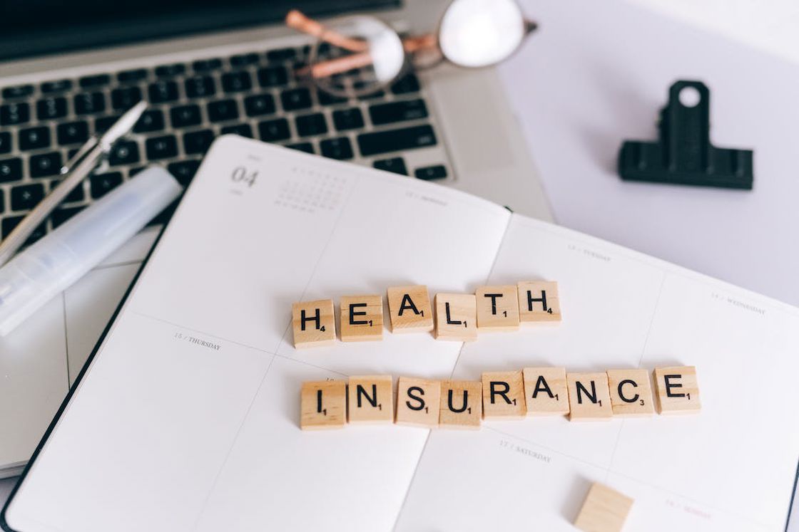 Wooden letter blocks spelling out the name "health insurance" placed on top of an opened daily organizer