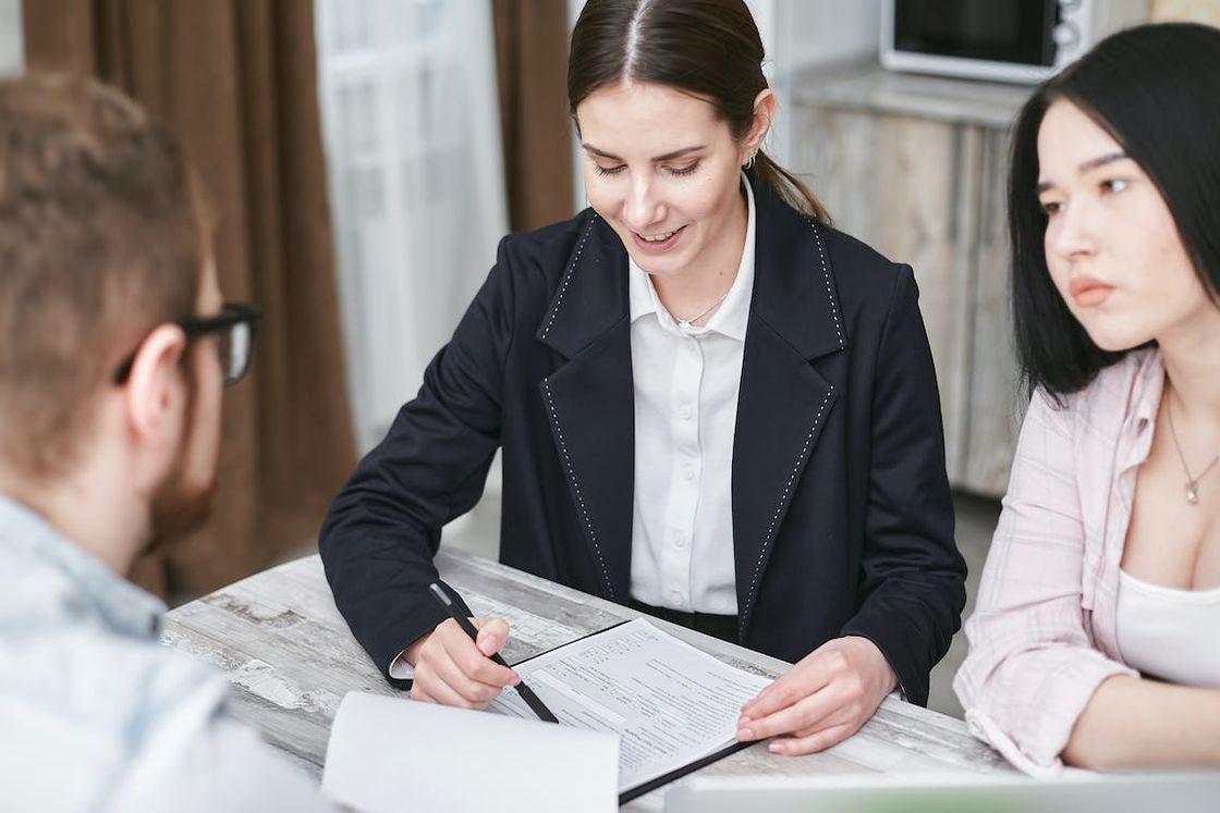 Woman reviewing the documents laid out on the table while her clients are listening