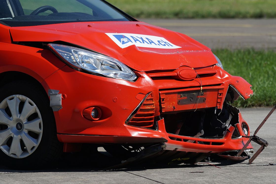 Front end of a red car almost falling off its frame after a car accident