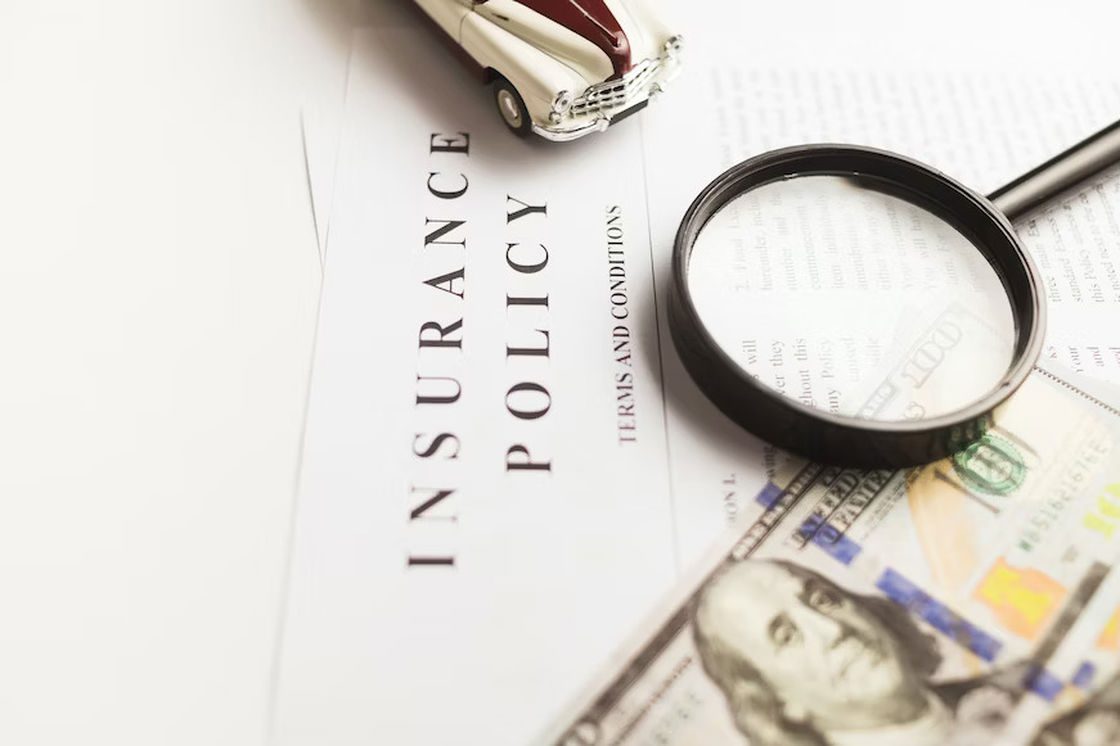 Magnifying glass on top of an insurance policy document right beside a dollar bill