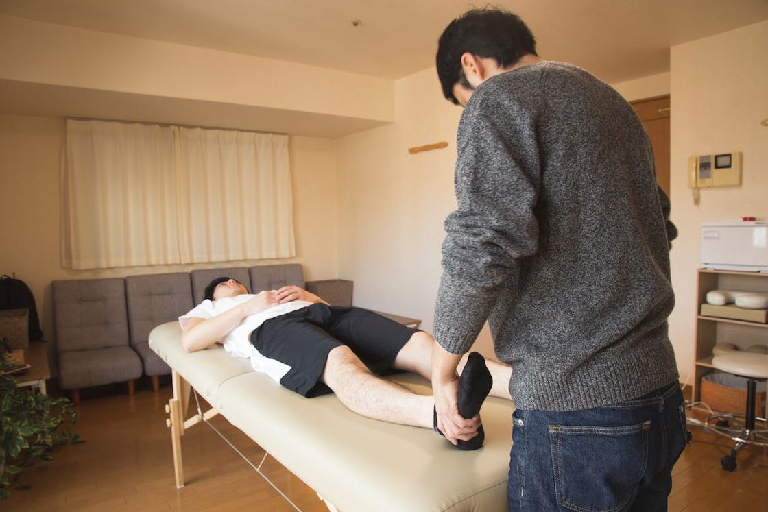 Therapist examining his patient's legs while he's lying down on the examination bed
