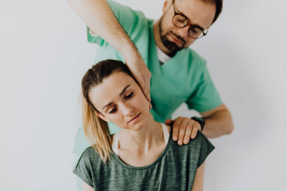 Doctor carefully tilting the head of a woman to check her neck injury
