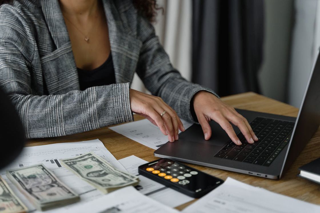 Woman using her laptop while dollar bills, papers and a calculator are placed on her table