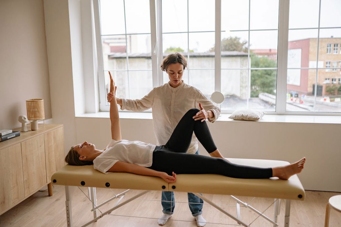 Woman lying on a therapy bed while her chiropractor stretches her arm and bends her legs