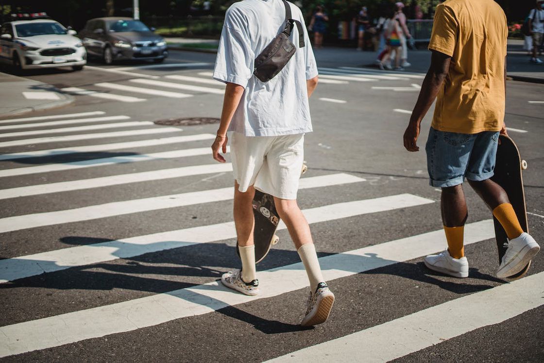 Two men holding skateboards while walking in a pedestrian crosswalk