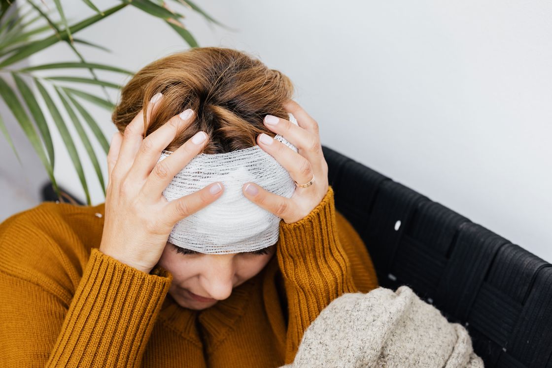 Woman with a bandaged head clutching her head with both her hands