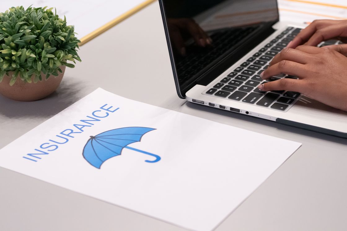 Paper with the word insurance and an image of an umbrella beside a person typing in a laptop