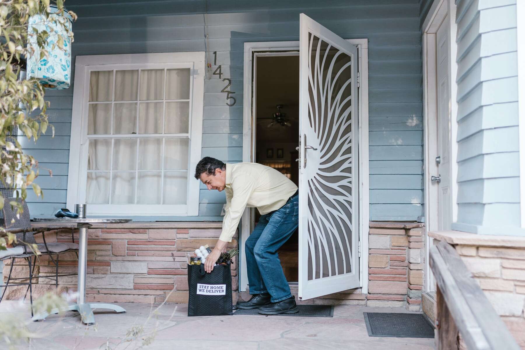 Man picking up a bag of groceries from his front door