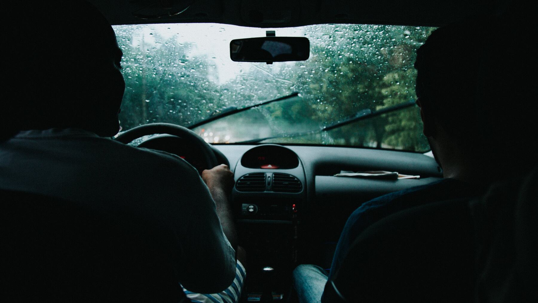 Man with a passenger driving a car on a rainy day