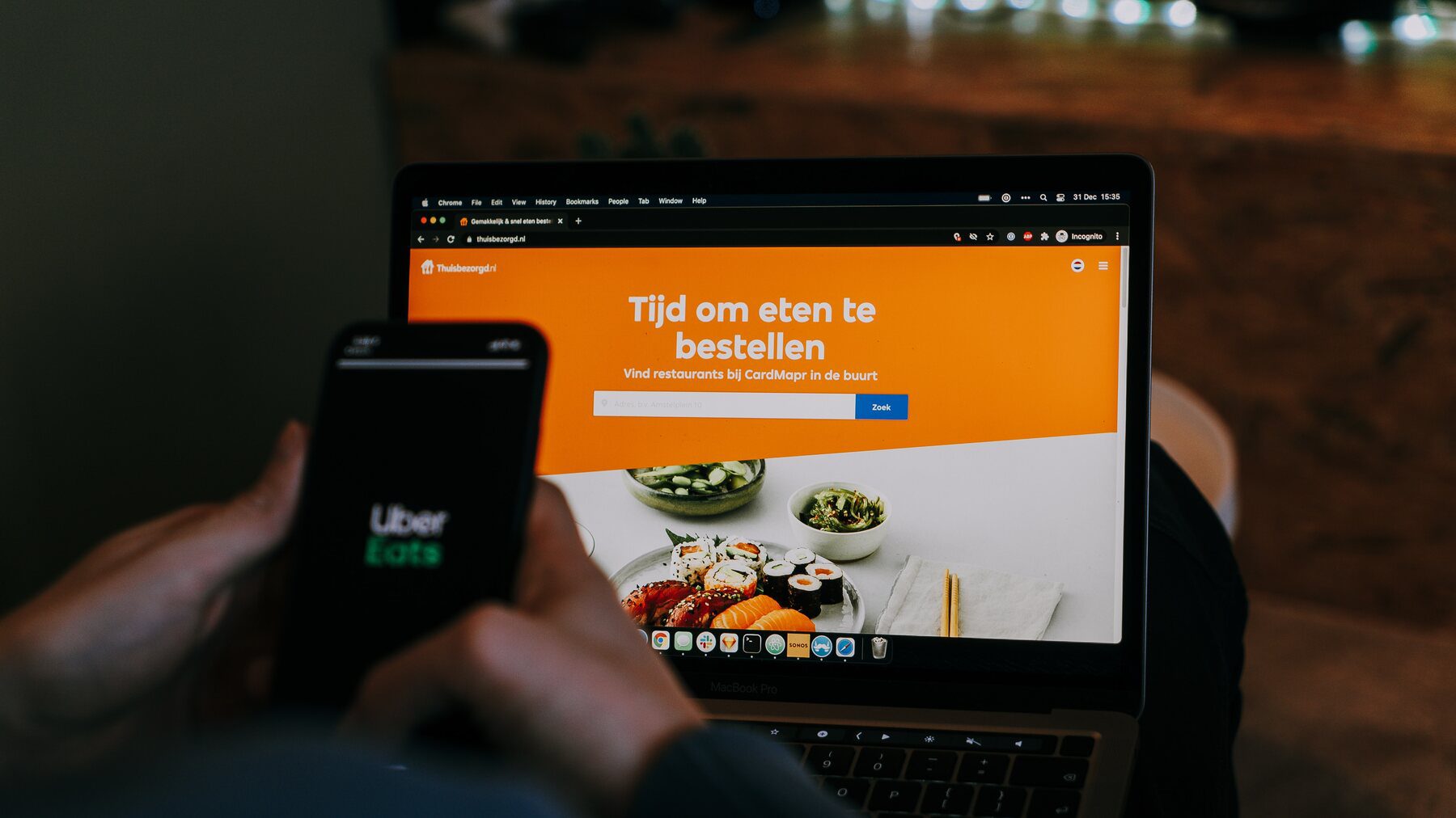 Man looking at the Uber Eats app on his phone while his laptop is on his lap