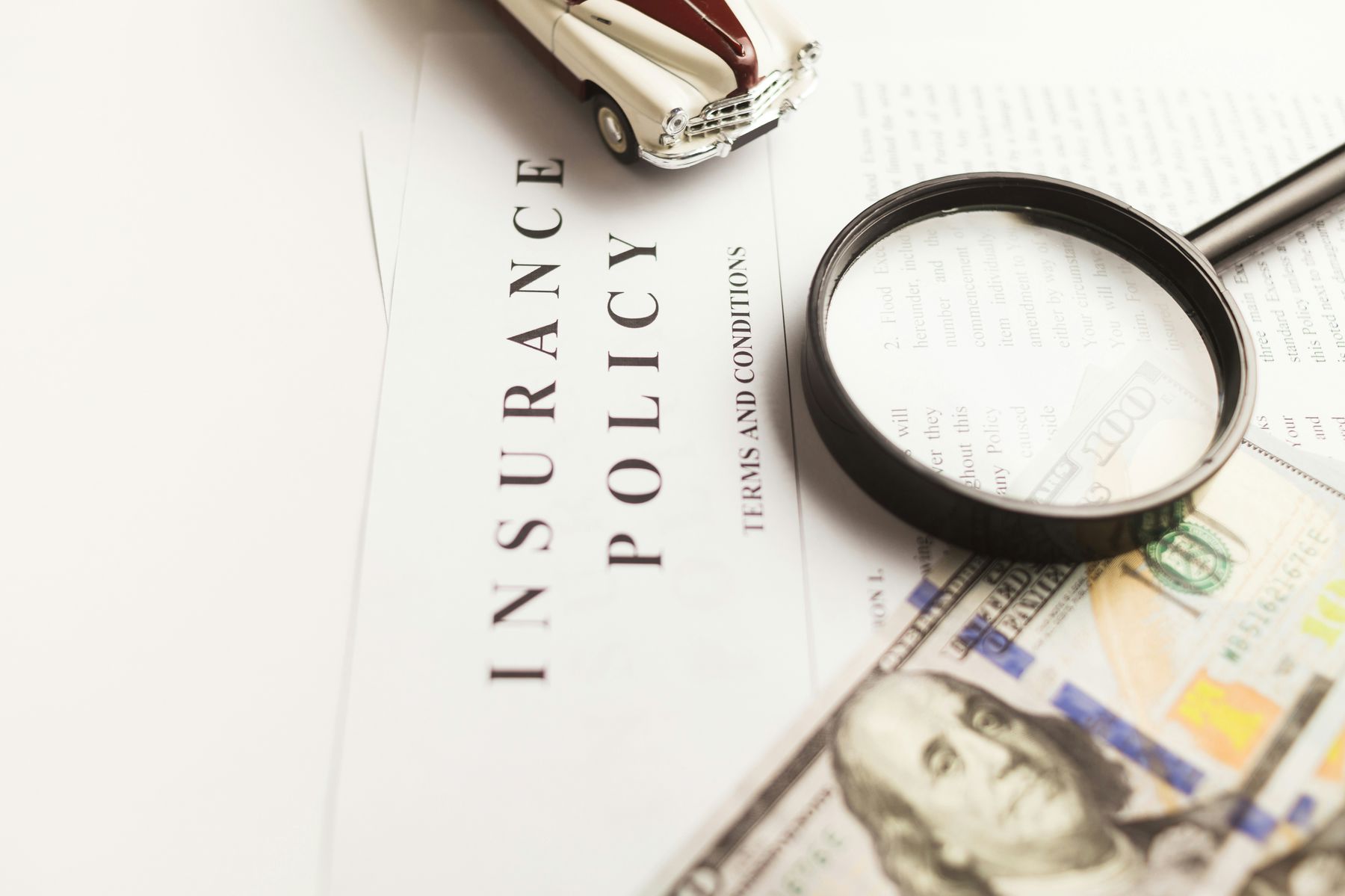 Magnifying glass and dollar bill on top of an insurance policy copy