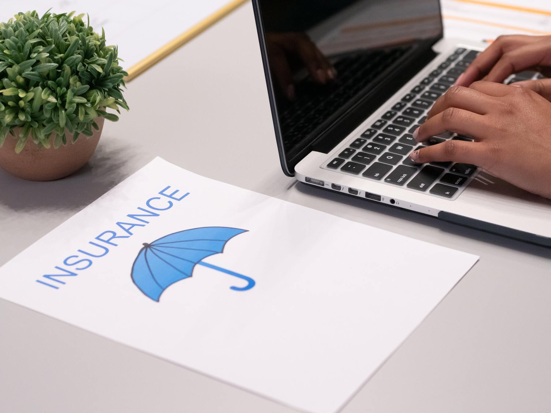 Person using a laptop with a piece of paper that has a printed text of "insurance" and a graphic image of an umbrella beside him