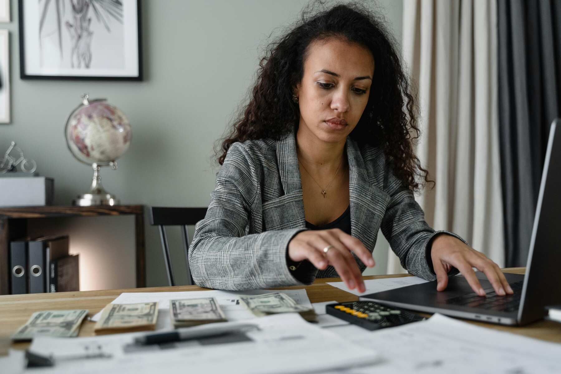 Woman using the calculator while typing in her keyboard, with money and papers on the table