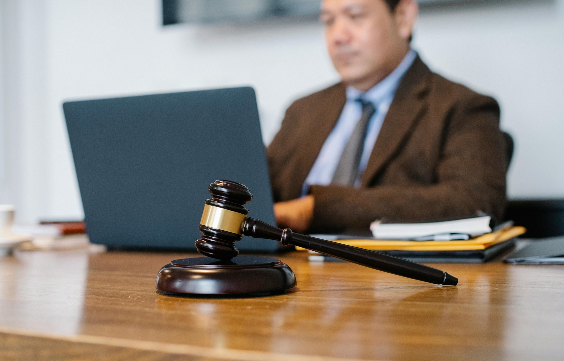Gavel and block on a table while the outline of a lawyer is seen on the background