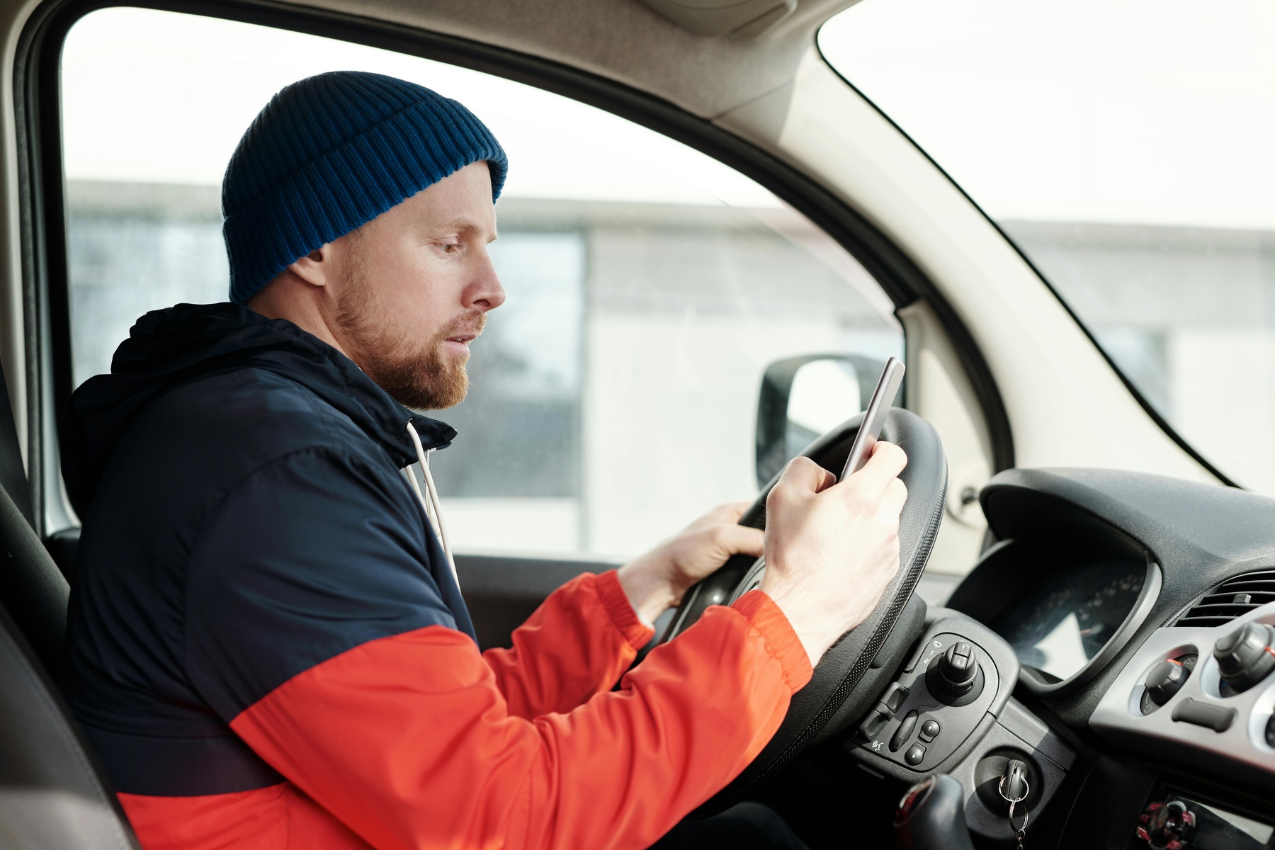 A man in a red and blue jacket using a smartphone while seated in a car