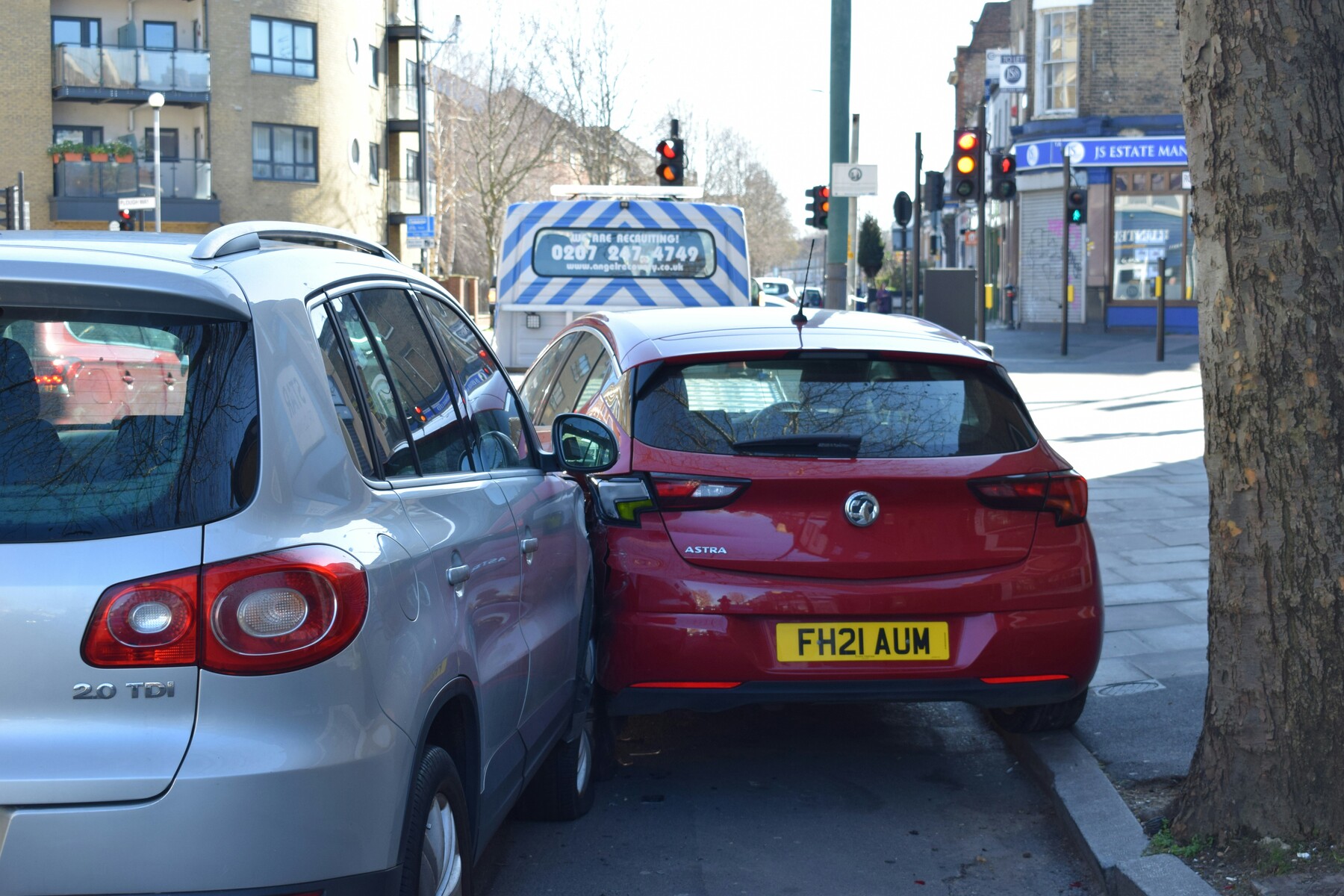 A gray car hitting a red car near the sidewalk