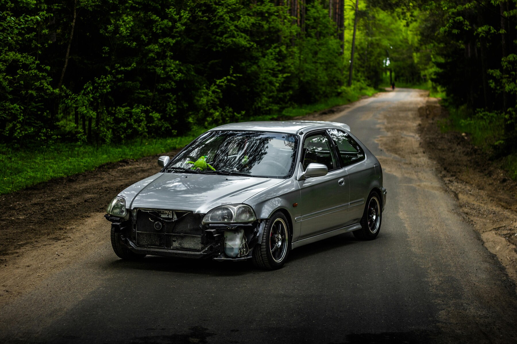 A silver car with a damaged front bumper parked on a rural road