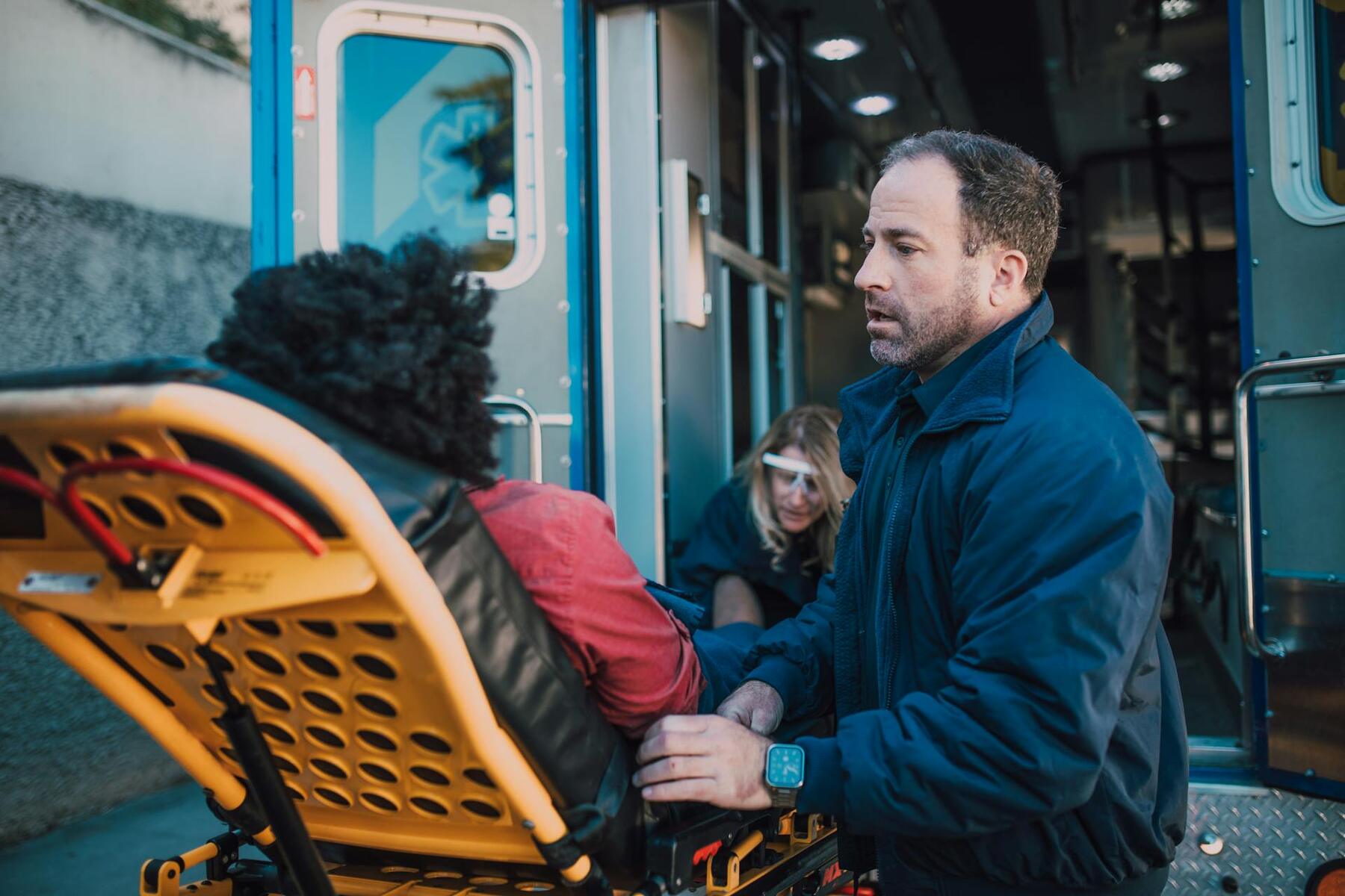 A man wearing a blue jacket converses with a man who is in a stretcher