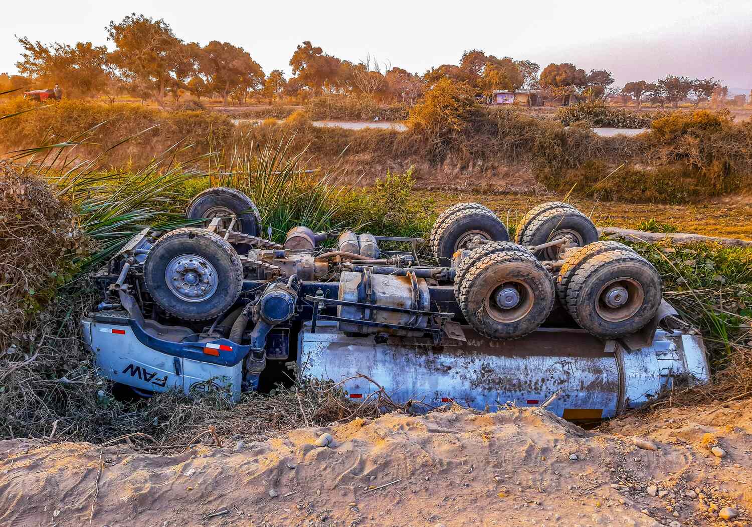 An overturned truck lying on its roof in a rural area during daylight.