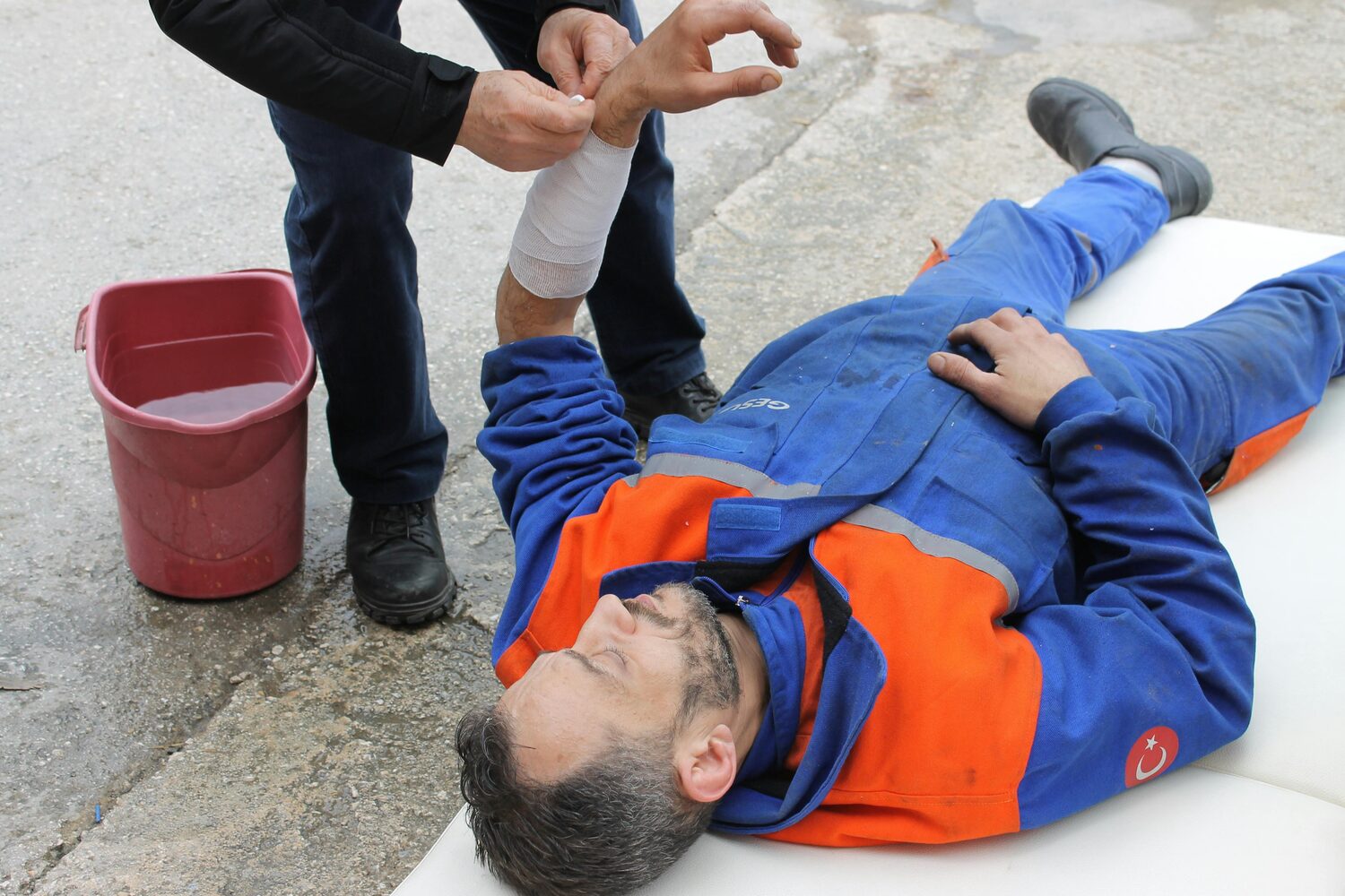 A man lying on the ground receiving medical attention on his arm.
